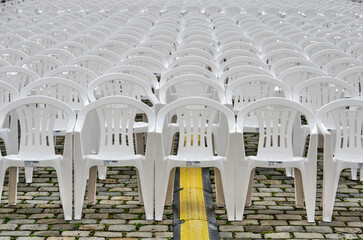 Rows of white plastic chairs on a cobblestone pavement with a cable tray