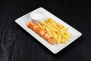 Grilled chicken shashlik meat with fried potatoes on white plate on black wooden background