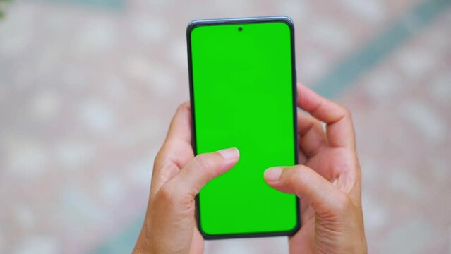 Female hand holding smartphone with green screen. Using mobile phone at home. Chroma key, close up Indian woman hand holding phone with vertical green screen.