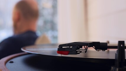 Close-up of a vinyl record spinning in a turntable. In the blurred background, an unrecognizable...