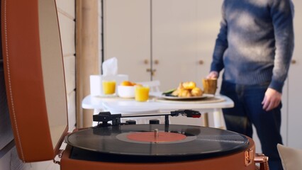 Fototapeta premium In the early morning, a man has breakfast and turns on a vinyl record player, music cheers up and charges with a good mood for the whole day. A man at home alone has breakfast and listens to music.