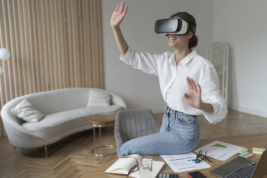 Businesswoman in VR headset on head touching 3d objects while working in modern office