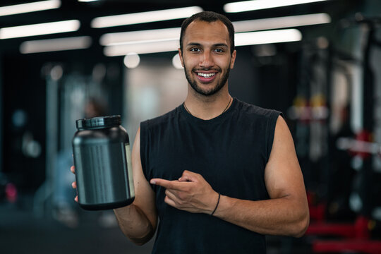 Handsome Black Male Athlete Advertising Fitness Supplements While Posing At Gym Interior