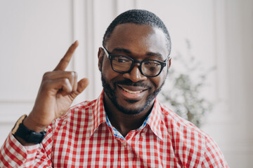 Smiling African ethnicity male English tutor in glasses raises hand points out with index finger up