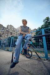 A teenage boy is sitting on the railing outside in the urban exterior.