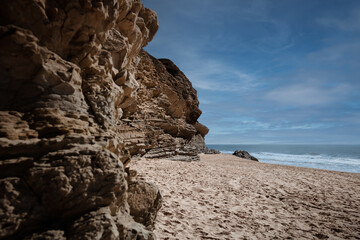 Fototapeta premium Praia da Murtinheira in Quiaios, Portugal, a quiet and wild beach away from the crowds. Close-up of rocky shore, sand and blue sky. Landscape photography