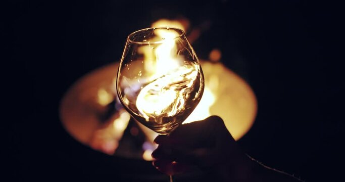 Tasting white wine at night. Glass of white wine slightly shaking against camp fire background. Winemaking in France, Provance. Slow motion shot, 4K