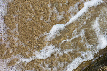 Beach sand sea water summer background. Sand beach desert texture. White foam wave sandy seashore top view.
