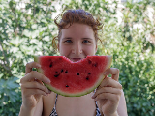 Smiling young woman holding ripe red watermelon slice with missing bite in both hands
