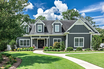 A large gray craftsman new construction house with a landscaped yard and leading pathway sidewalk - Powered by Adobe