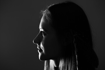 Close-up woman with feathers in her hairs dark profile portrait. Model face partly illuminated by light. Selective focus and image with shallow depth of field. Black and white image