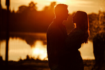 silhouette of loving couple hugging on the lake at sunset. Beautiful young couple in love walking...