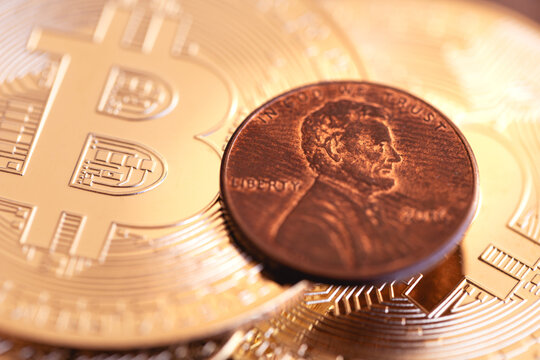 Moedas douradas de Bitcoin e uma moeda de US 1 centavo em um mobili&aacute;rio de madeira em macrofotografia. Criptomoeda, m&eacute;todo de pagamento e risco.
