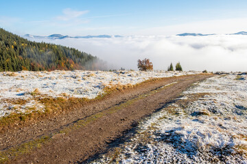rural off road from peak to mountains in clouds at sunrise in autumn with first snow. Beautiful landscape with Ukrainian Carpathians, forest, sky.