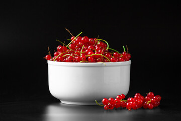 Branches of red currant in a white plate on a dark background