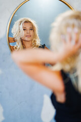 an attractive blonde in a black dress looks at the reflection in the mirror 