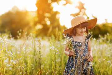 Fototapeta na wymiar smiling child girl in a big mommys straw hat with bouquet of wildflowers in a green grassy meadow on summer sunny day. Happy childhood concept. Copy space.