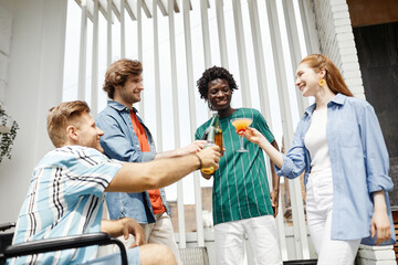 Low angle view at diverse group of friends with person in wheelchair clinking glasses while enjoying party at outdoor terrace lit by sunlight