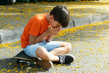 Boy sitting on skateboard in the street surrounded by pollen on the ground. Flower pollen allergy...