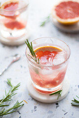 Grapefruit lemonade in a glass with ice cubes and rosemary. Summer cold drink on terrazzo background