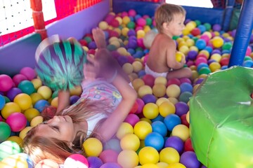 The older sister plays with her younger brother and throws small balls at him while sitting in the...