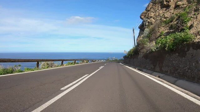4K POV footage of car driving along countryside road through beautiful mountain landscape with rocks, cliffs, village, Atlantic ocean on horizon. Typical volcanic island landscape. Tenerife, Spain