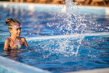A girl in a bright bathing suit swims with an inflatable ball in a pool with clear water on a summer evening
