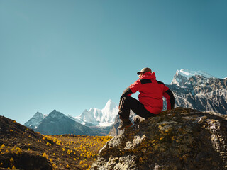 asian man sitting on top of rock looking at view with Mount Yangmaiyong (or Jampayang in Tibetan) in the distance in Yading, China