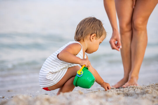 The kid collects shells and pebbles in the sea on a sandy bottom with his mother under the summer sun on vacation