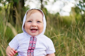 Portrait of a joyful boy in Ukrainian traditional national clothes - vyshyvanka on a green background. Ukraine, child in nature	