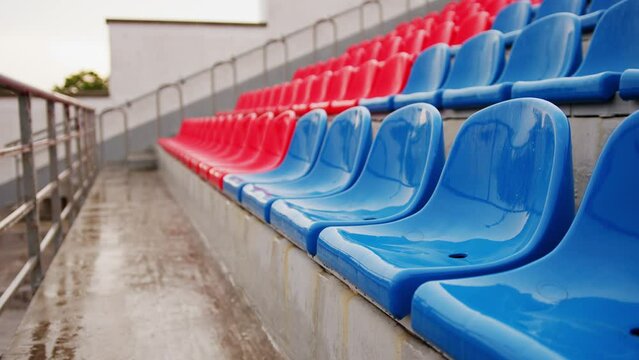 Empty bleacher in sports stadium in rainy weather. Colored wet seats in street stadium. It's raining. Close up.