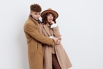 a cute couple is standing on a light background dressed in coats and sweaters, a man and a woman are looking down confusedly hugging each other