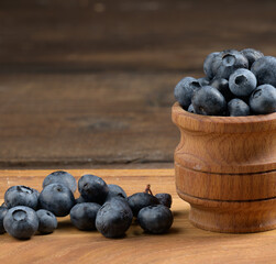 Ripe blueberries in a wooden bowl on the table, black background