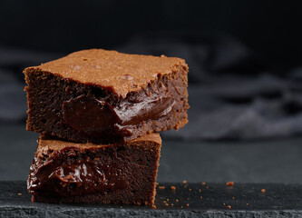 Baked pieces of chocolate brownie pie on black table, delicious dessert