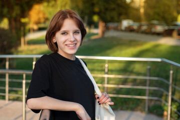 A happy teenage girl is smiling and resting in the park, she is coming back from the dentist where she was fitted with metal braces on the lower and upper jaw.  Healthy dental concept