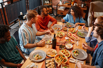 High angle view at diverse group of young people enjoying dinner party at table in cozy setting
