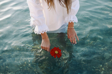 Beautiful female hands holding a red gerbera, blue sea water background, copy space