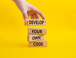 Develop your own code symbol. Concept words Develop your own code on wooden blocks. Beautiful yellow background. Businessman hand. Business and Develop your own code concept. Copy space.