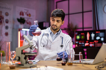 Yong indian male scientist working with test tubes wearing lab coat working in laboratory while...