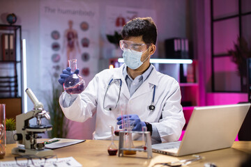 Positive male arab scientist or medical in lab coat holding test tube with reagent, laboratory glassware containing chemical liquid. Microscope, Biochemistry laboratory research.