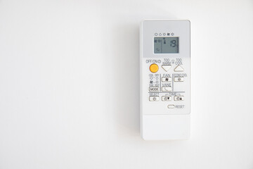 Air conditioner control hanging on a white wall, with 19 degrees on the display, as recommended by...