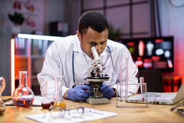 Young african american male researcher looking at the microscope analyze science, forensics, microbiology, biochemistry, genetics, oncology, laboratory.