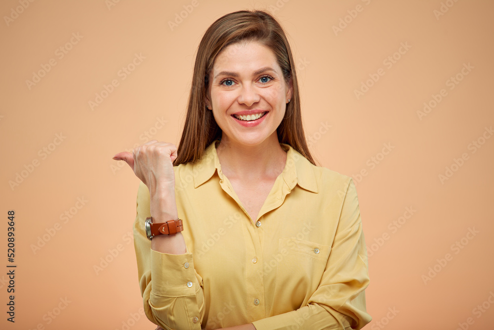 Wall mural smiling woman pointing finger at side, isolated portrat on studio yellow background.