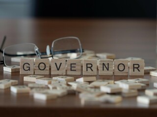 governor word or concept represented by wooden letter tiles on a wooden table with glasses and a...