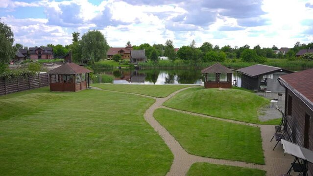 Wide shot beautiful landscape on eco-resort with wooden biuldings green meadow and lake. Scenics in tourist resort outdoors. Tranquility and eco-tourism concept