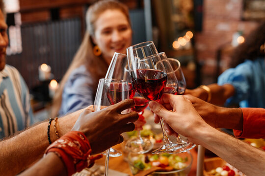 Close up of young people holding wine glasses and toasting while celebrating together at table during dinner party