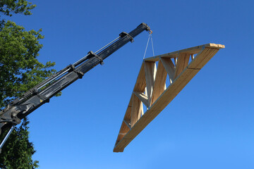 Lifting roof trusses by truck-mounted crane on hot summer day - obrazy, fototapety, plakaty