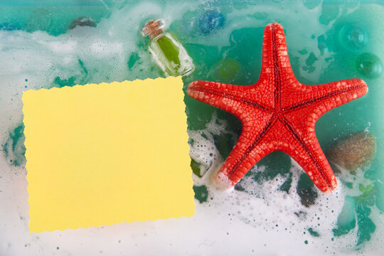 Message on paper in sea, ocean water. Bright red starfish and small glass ottle in foam, stones on bottom. Top view, flatly, copy spave for text. Blank paper greeting card