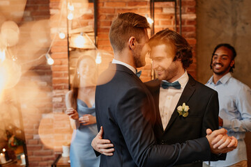 Dreamy portrait of young gay couple dancing together during wedding reception with lens flare