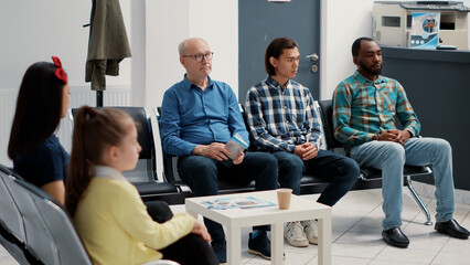 Diverse group of people sitting together in hospital waiting room, preparing to meet with general...